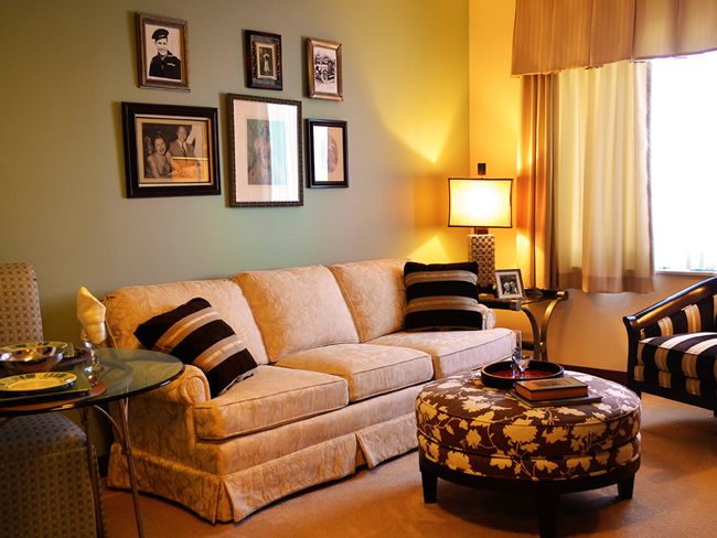 A cozy living room with a beige sofa, patterned ottoman, and decorative wall art.