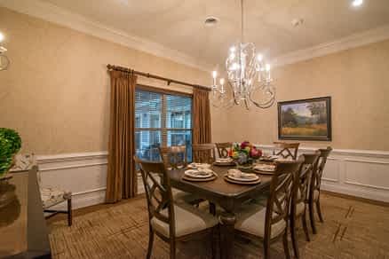 A warmly lit dining room featuring a wooden table set for dinner, surrounded by chairs and illuminated by an elegant chandelier.