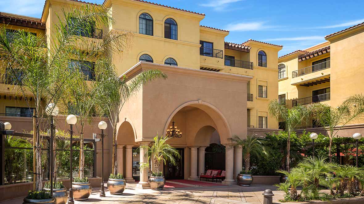 A Mediterranean-style hotel exterior with palm trees.