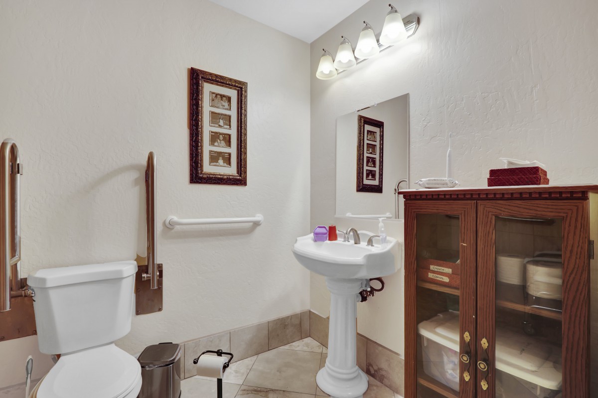 A well-lit bathroom with a pedestal sink, toilet, wooden cabinet, and wall art.