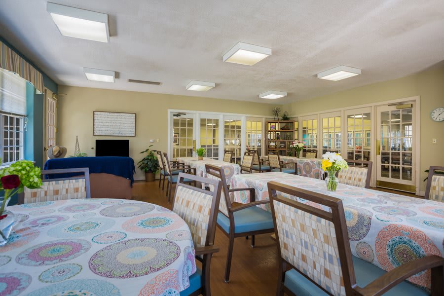 A well-lit dining room with multiple tables and chairs, featuring decorative elements and indoor plants.