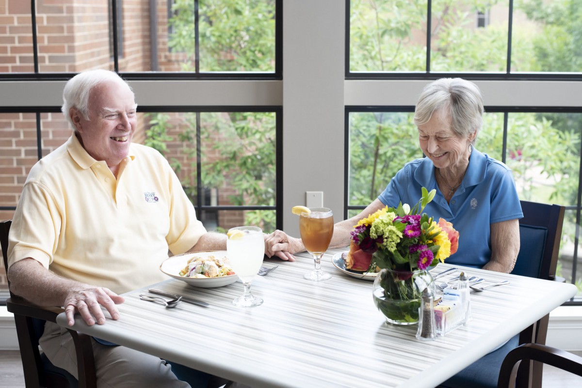 An elderly couple enjoying a meal together at a restaurant, sitting at a table with colorful flowers.