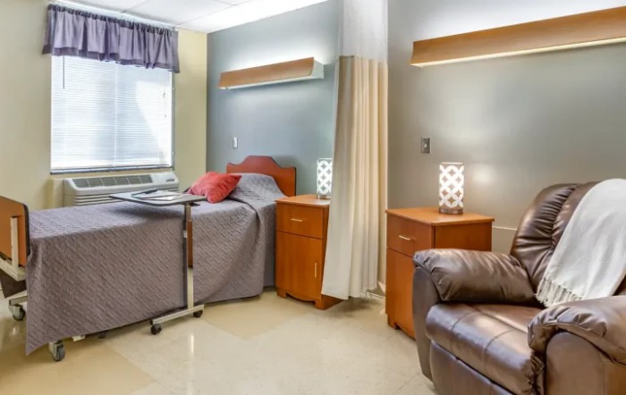 A clean and well-lit hospital room with a bed, bedside tables, and comfortable seating.