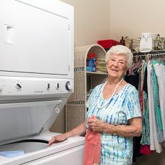An elderly woman doing laundry in a laundry room.