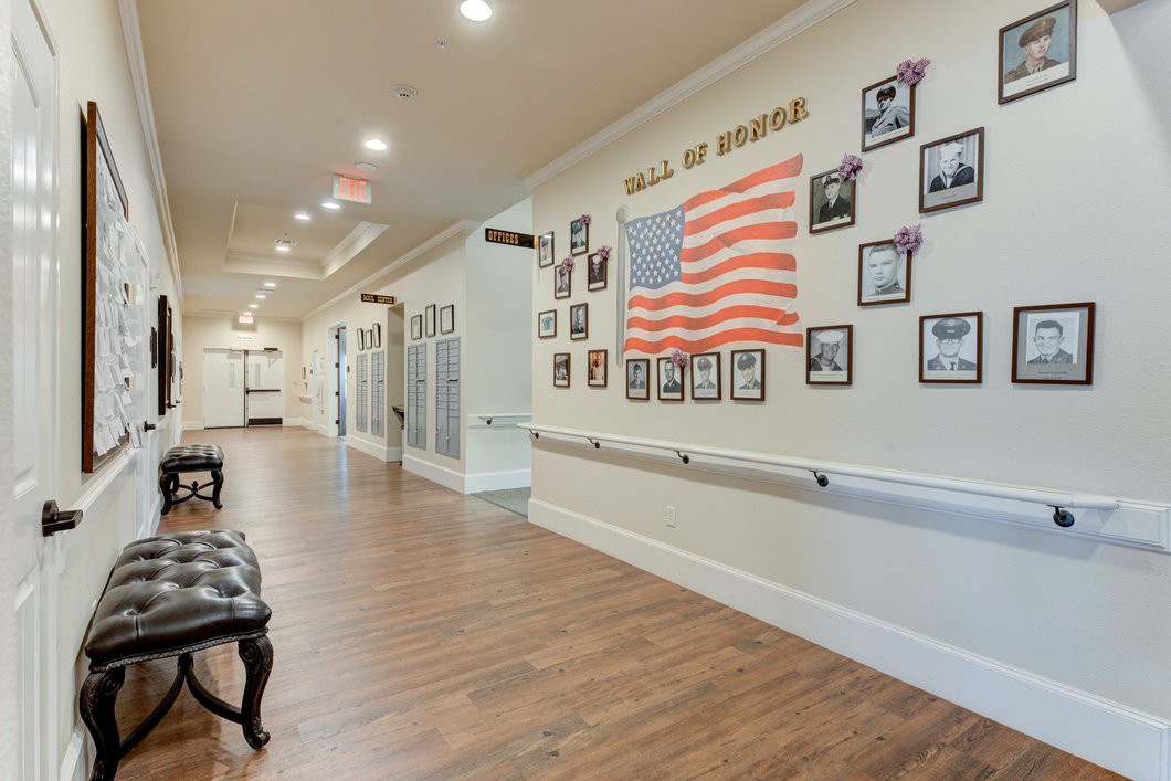 A hallway with an American flag and photos displayed on the wall, featuring a wooden floor and ceiling lights.