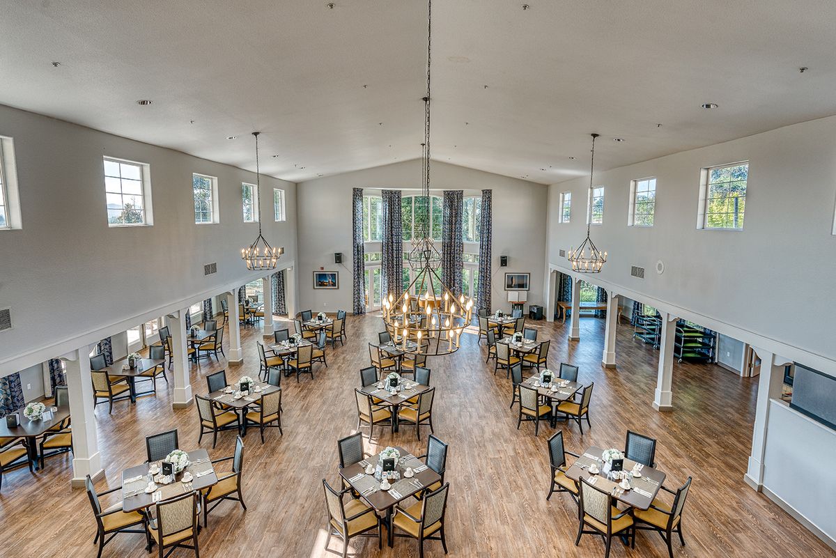 A spacious and elegant dining area featuring multiple tables, chairs, and chandeliers.