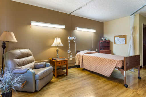 A well-lit patient room featuring a bed, recliner chair, and comfortable furnishings.