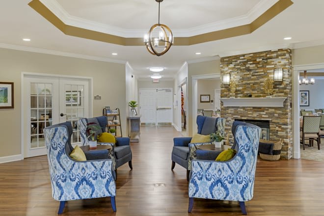 A cozy living room with patterned chairs, a stylish chandelier, and a stone fireplace.