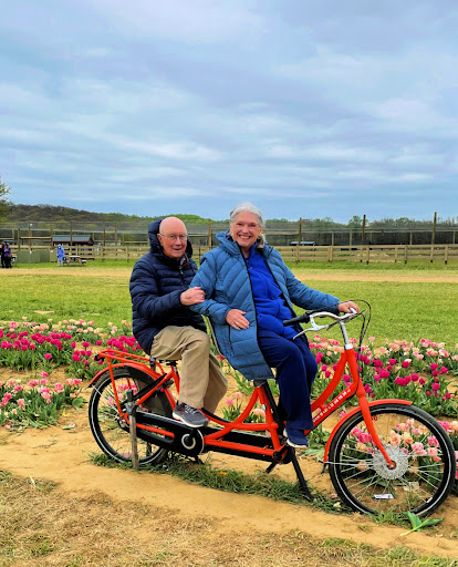 A joyful couple enjoying a ride on a tandem bike amidst blooming flowers.