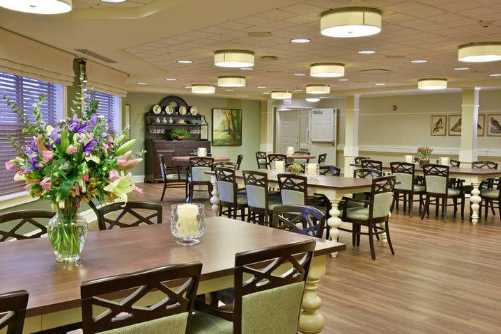 A well-lit dining room with neatly arranged tables and chairs, featuring floral decorations.