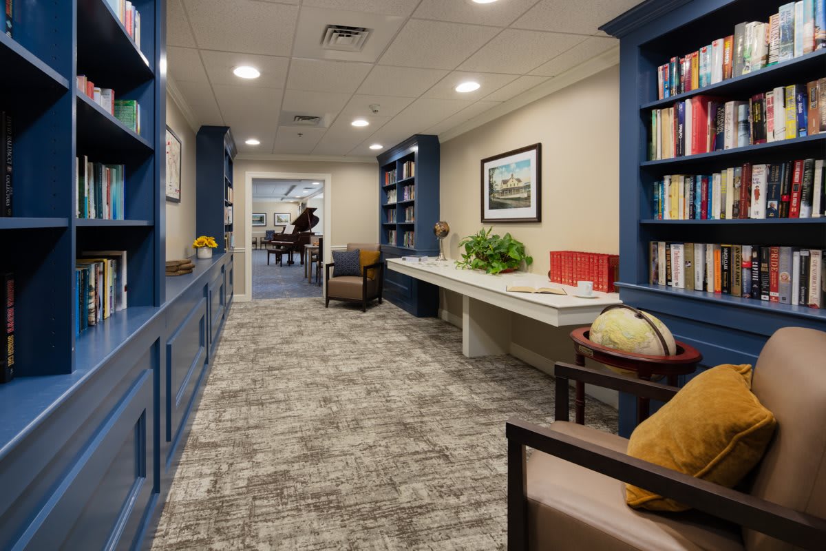 A cozy hallway with blue bookshelves, seating, and a globe, leading to another room.