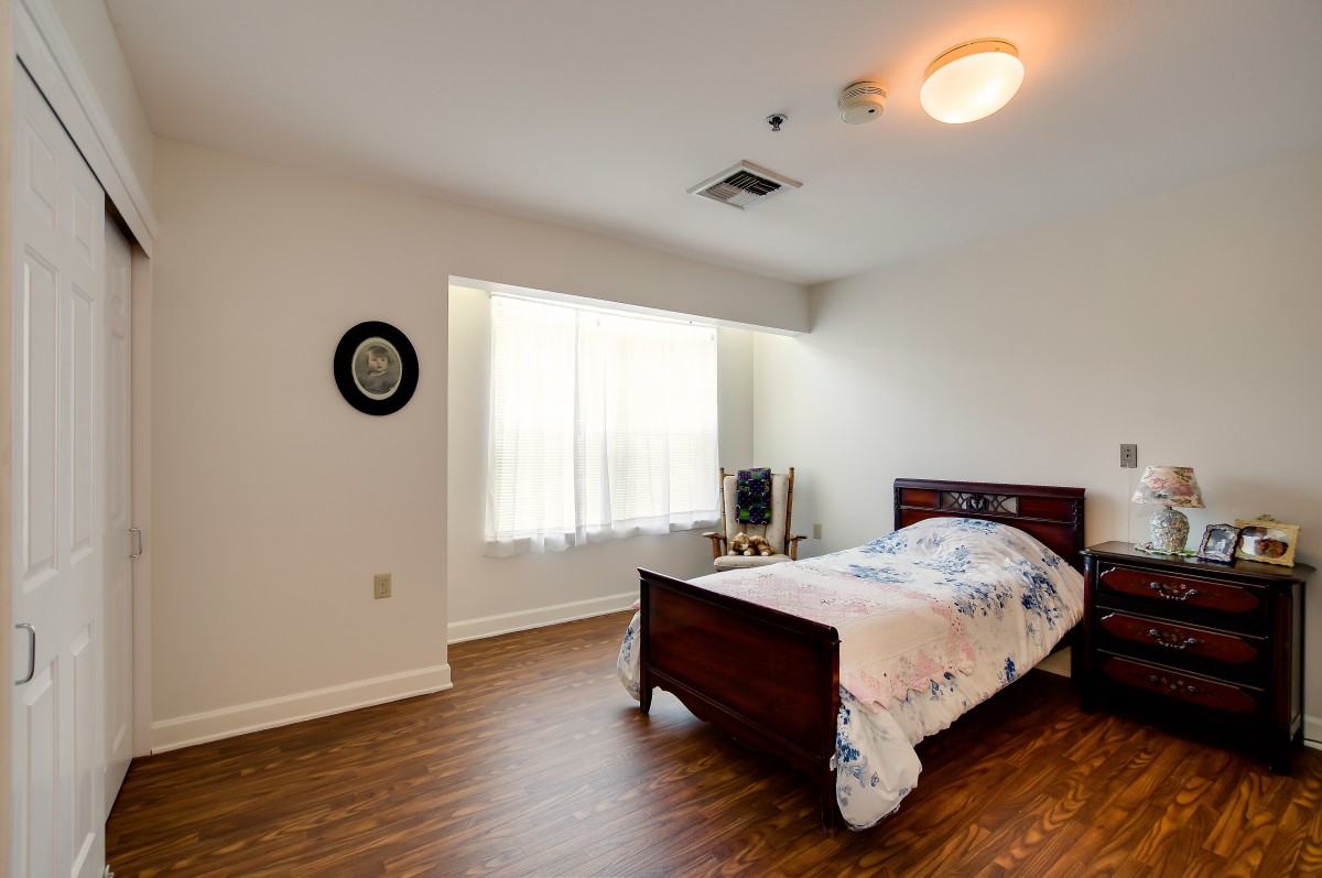 A minimalist bedroom with a single bed and wooden flooring, featuring a large window and simple decor.