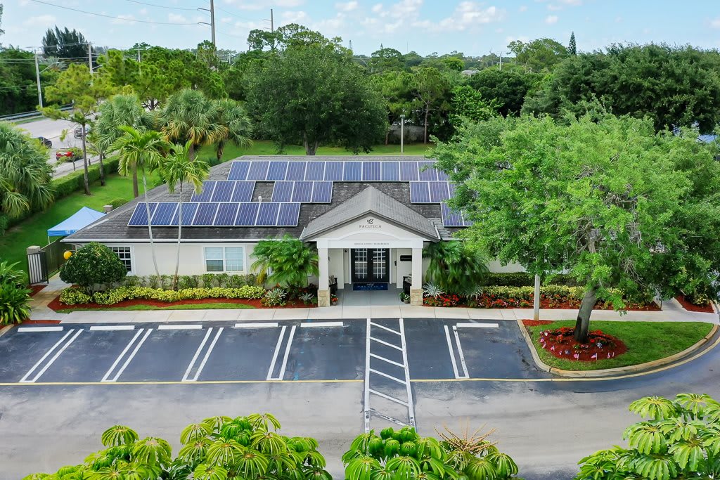 A building with a solar panel roof, surrounded by lush greenery and a neatly organized parking lot.