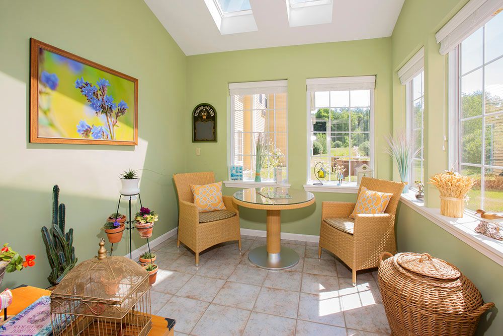 A bright sunroom featuring wicker chairs and a glass table, with natural light streaming in through skylights and windows.