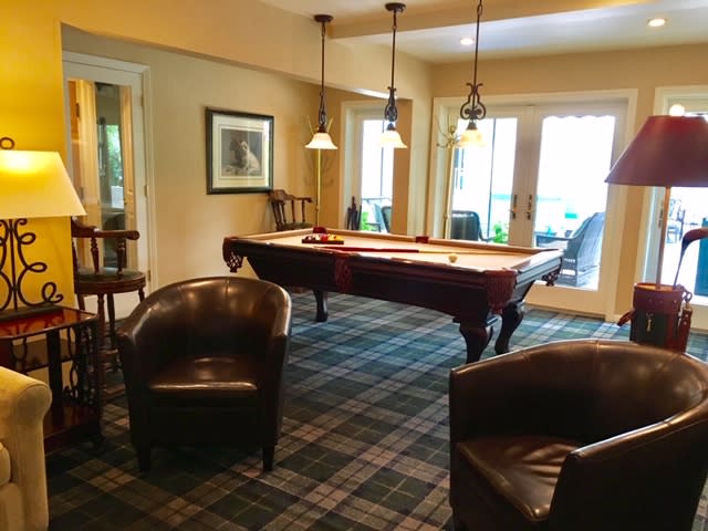 A cozy billiards room featuring a pool table, leather chairs, and elegant hanging lights.