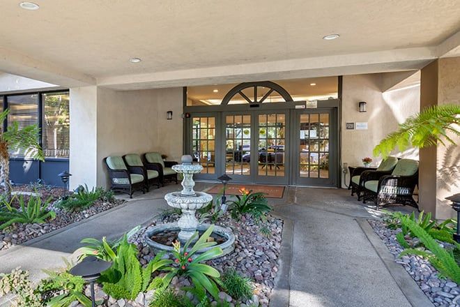 An inviting entrance with a fountain and cozy seating area surrounded by greenery.