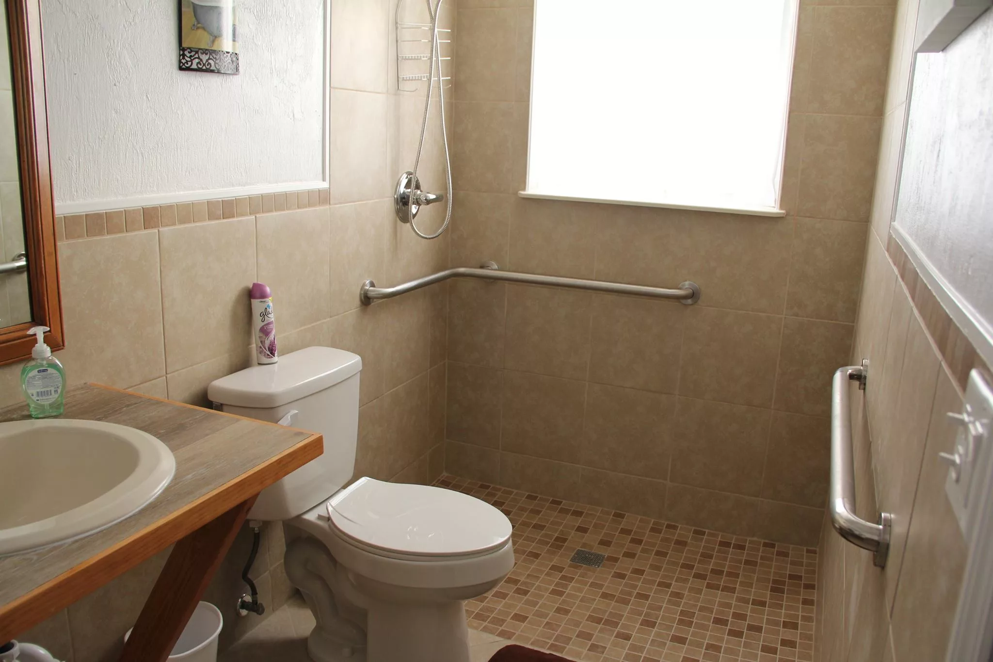A bathroom with a toilet, shower area, and grab bar, featuring tiled walls and a window.