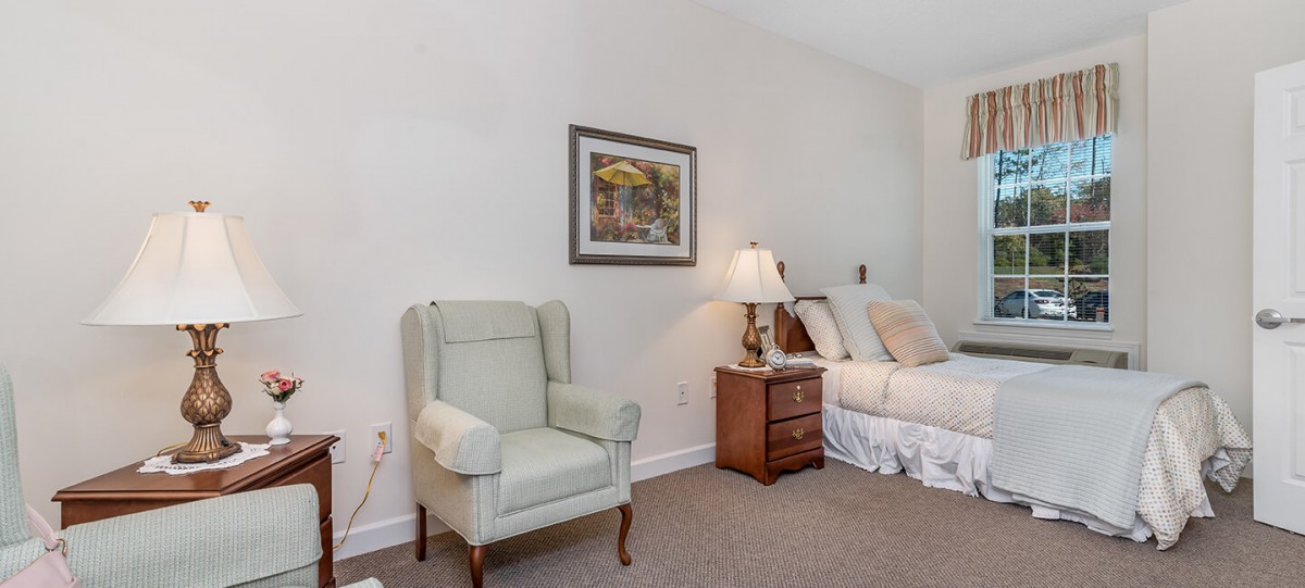 A cozy bedroom featuring an armchair, bed, bedside table, and a wall painting.