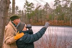 A couple is bird watching by a lake in a forest during winter.