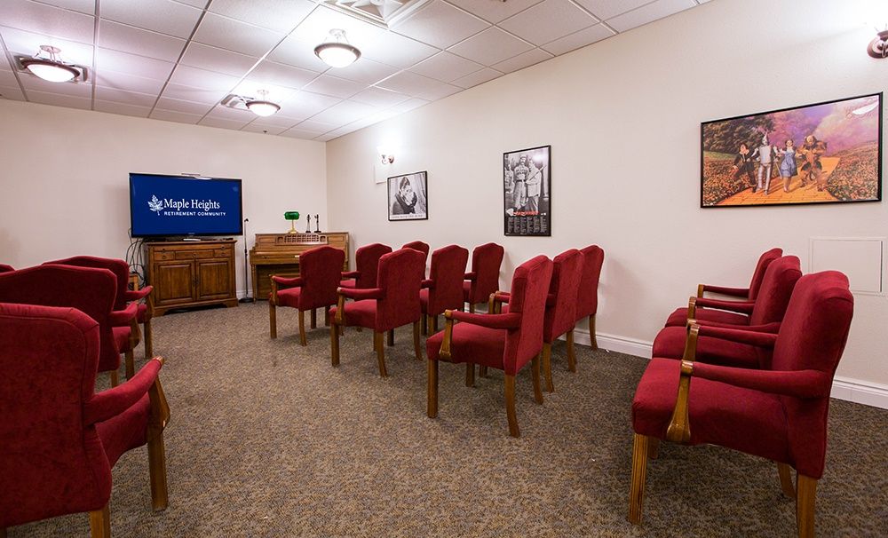 A small, organized room with red chairs arranged in rows facing a television.