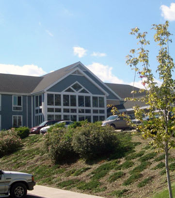 A suburban house with a sloped grassy lawn and parked cars under a clear blue sky.