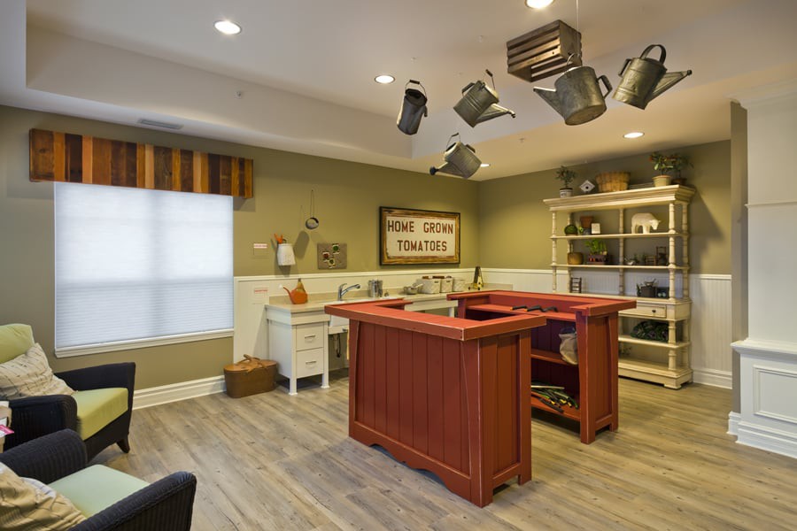 A cozy kitchen featuring a central island counter with hanging pots and pans, wooden flooring, and neatly organized shelves.