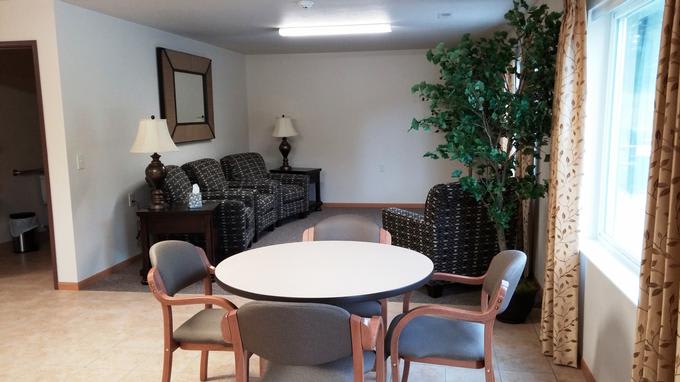 A cozy living room with seating area, a round table surrounded by chairs, and decorative elements like a lamp and a large indoor plant.