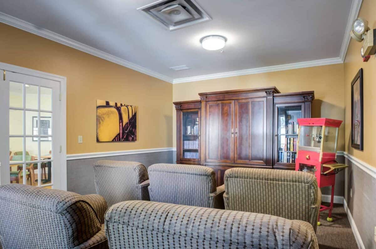 A cozy living room with several chairs, a wooden cabinet, and a piece of artwork on the wall.