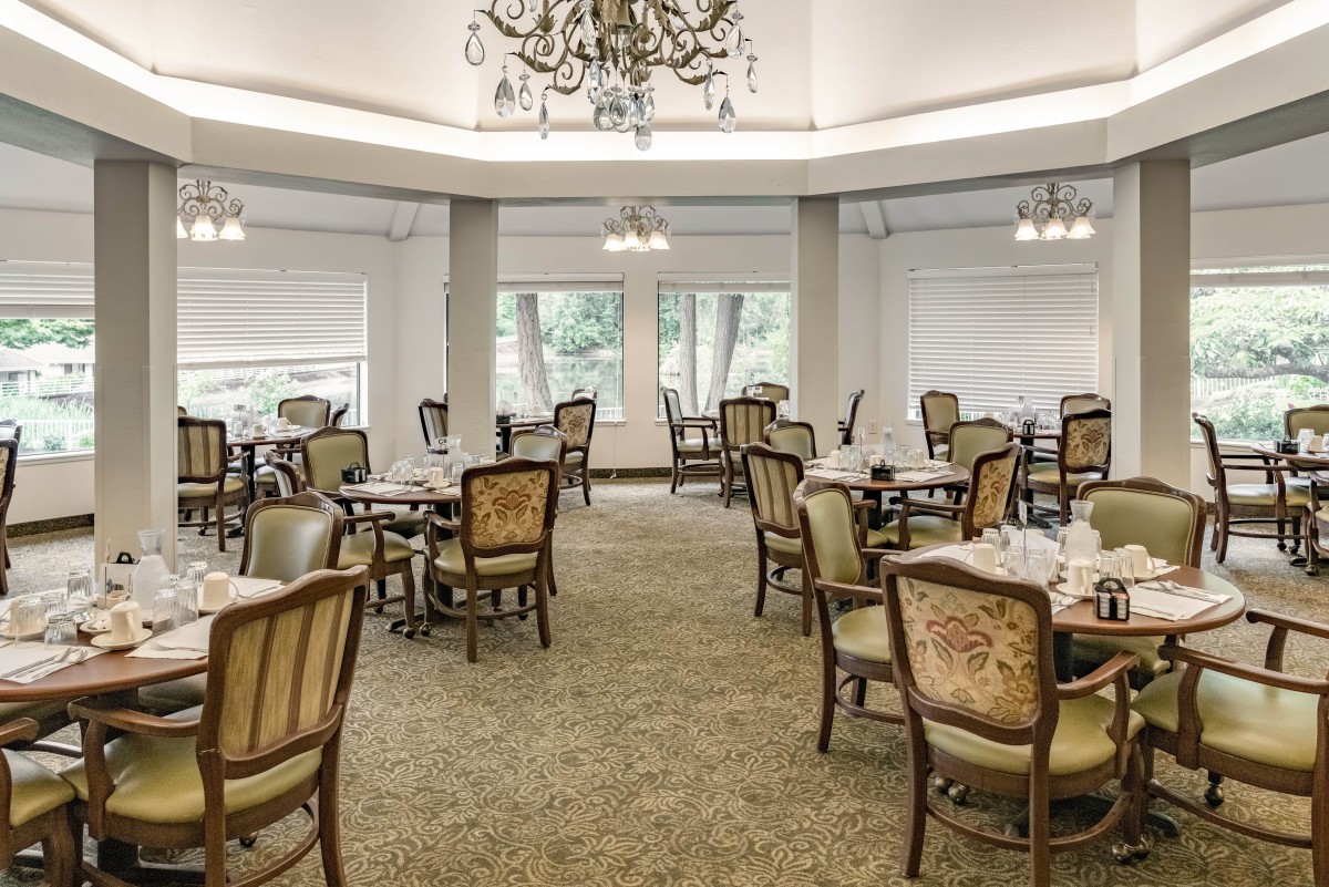 A spacious dining room with elegant furniture and a central chandelier.