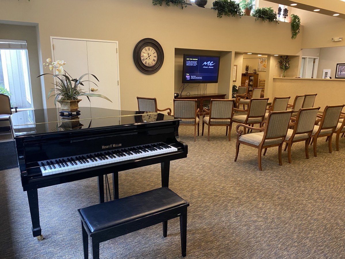 A cozy room with a piano, seating area, and a TV on the wall.