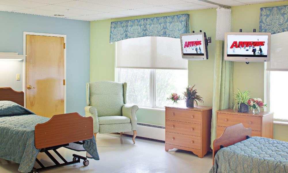 A hospital room with a bed, chair, dresser, and television.