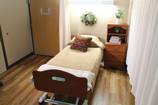 A cozy and well-organized patient room featuring a hospital bed, wooden furniture, and warm decor.