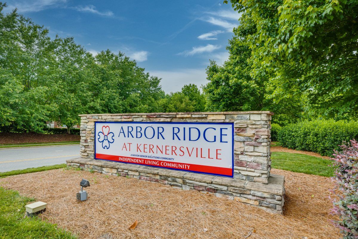 A stone sign for Arbor Ridge at Kernersville surrounded by trees and a clear blue sky.
