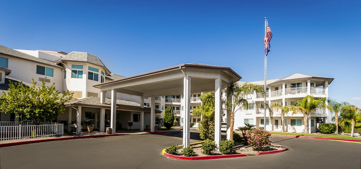 A modern building entrance with a covered driveway and landscaped surroundings under a clear blue sky.