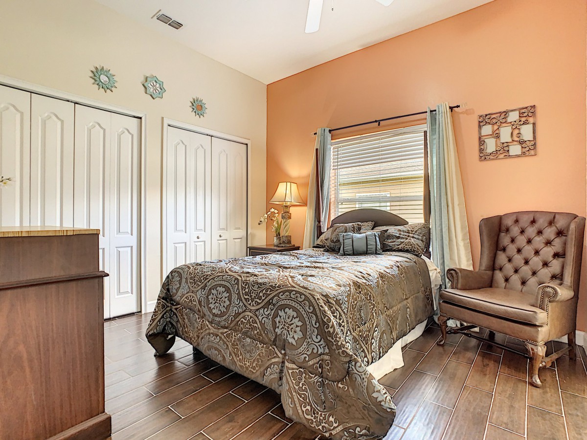 A cozy bedroom with a stylish decor, featuring a bed, chair, and lamp near the window.