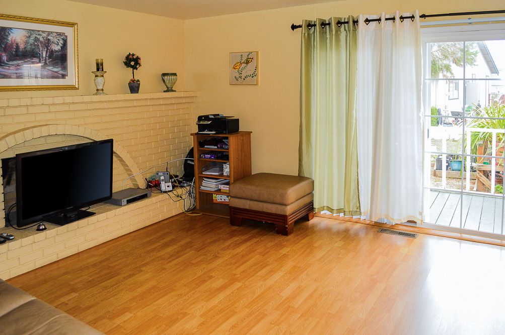 A minimalist living room featuring a wooden floor, television, shelving, and green curtains.