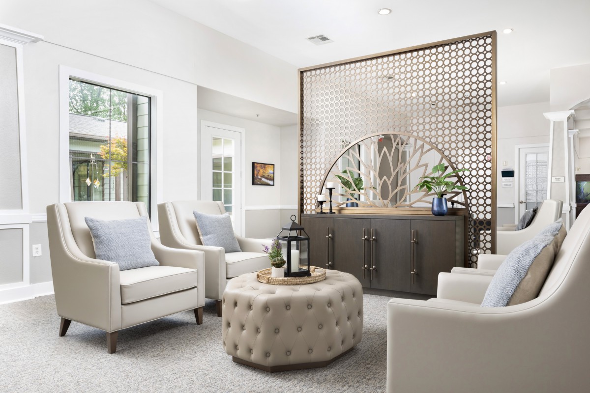 A modern living room with neutral tones featuring comfortable armchairs, a tufted ottoman, and decorative accents.