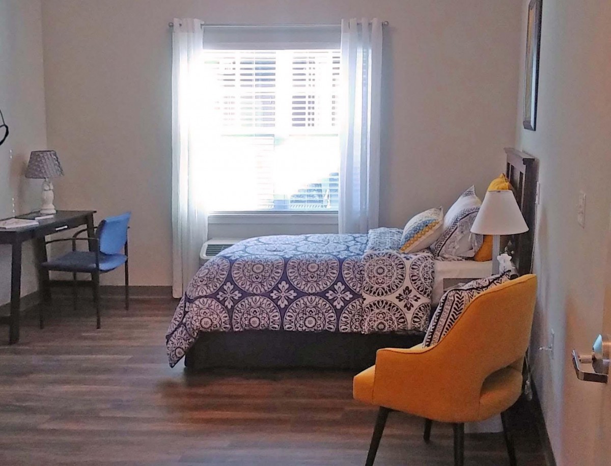 A cozy bedroom featuring a comfortable bed, stylish chair, and natural light from the window.
