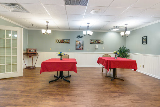 A spacious restaurant interior featuring two tables with red tablecloths, decorative artwork on the walls, and warm lighting.