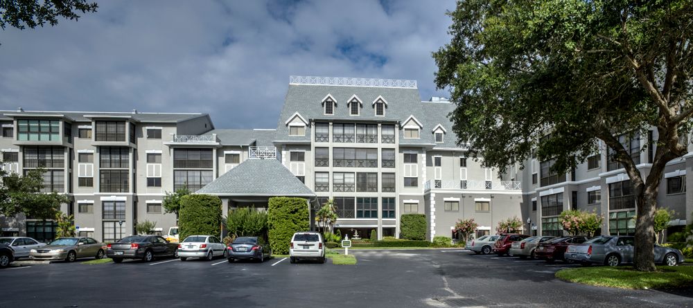 A large hotel building with a parking lot in front, surrounded by trees under a partly cloudy sky.