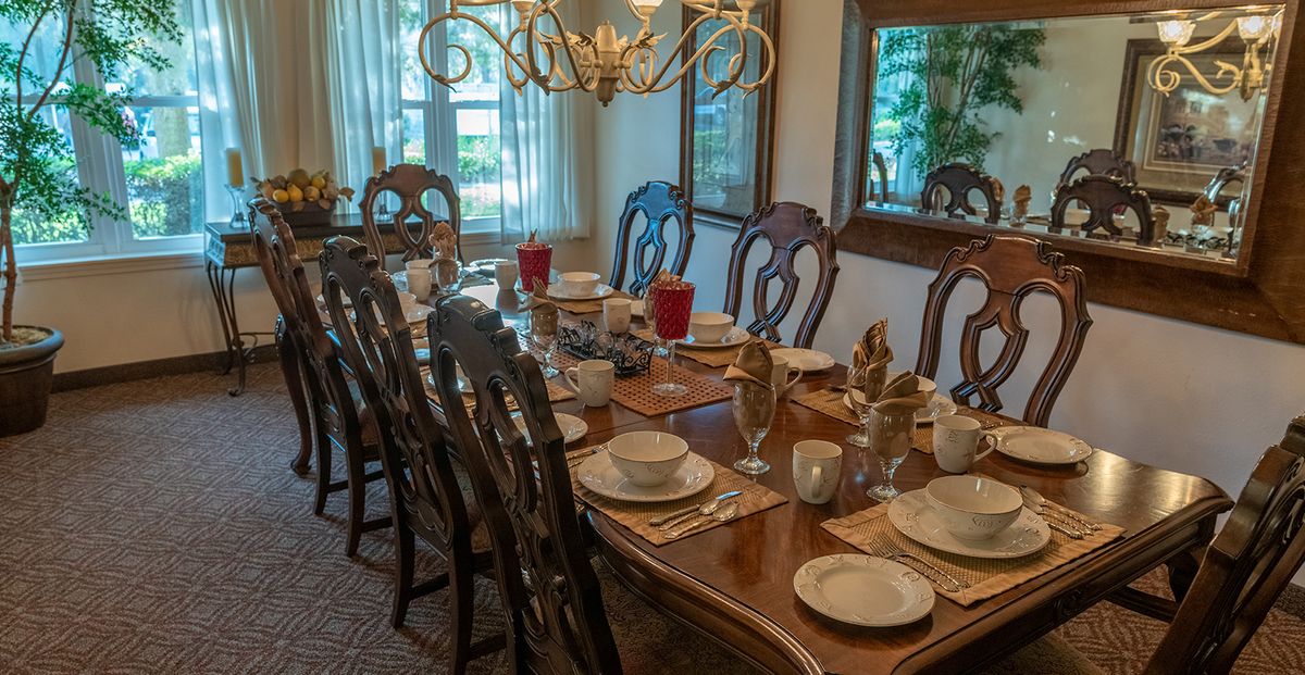 A formal dining room with an elegantly set table, complete with plates, glasses, and a chandelier overhead.