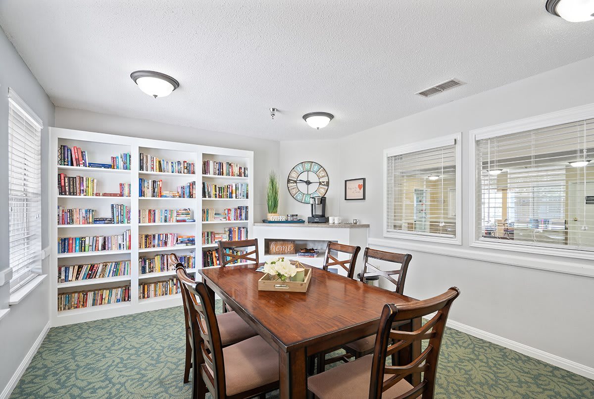 A cozy library room featuring a large table surrounded by chairs and shelves filled with books.