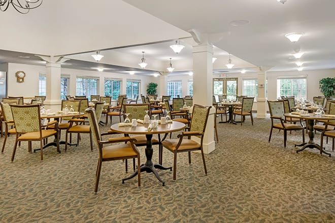 An empty dining room with neatly arranged tables and chairs, illuminated by overhead lights.