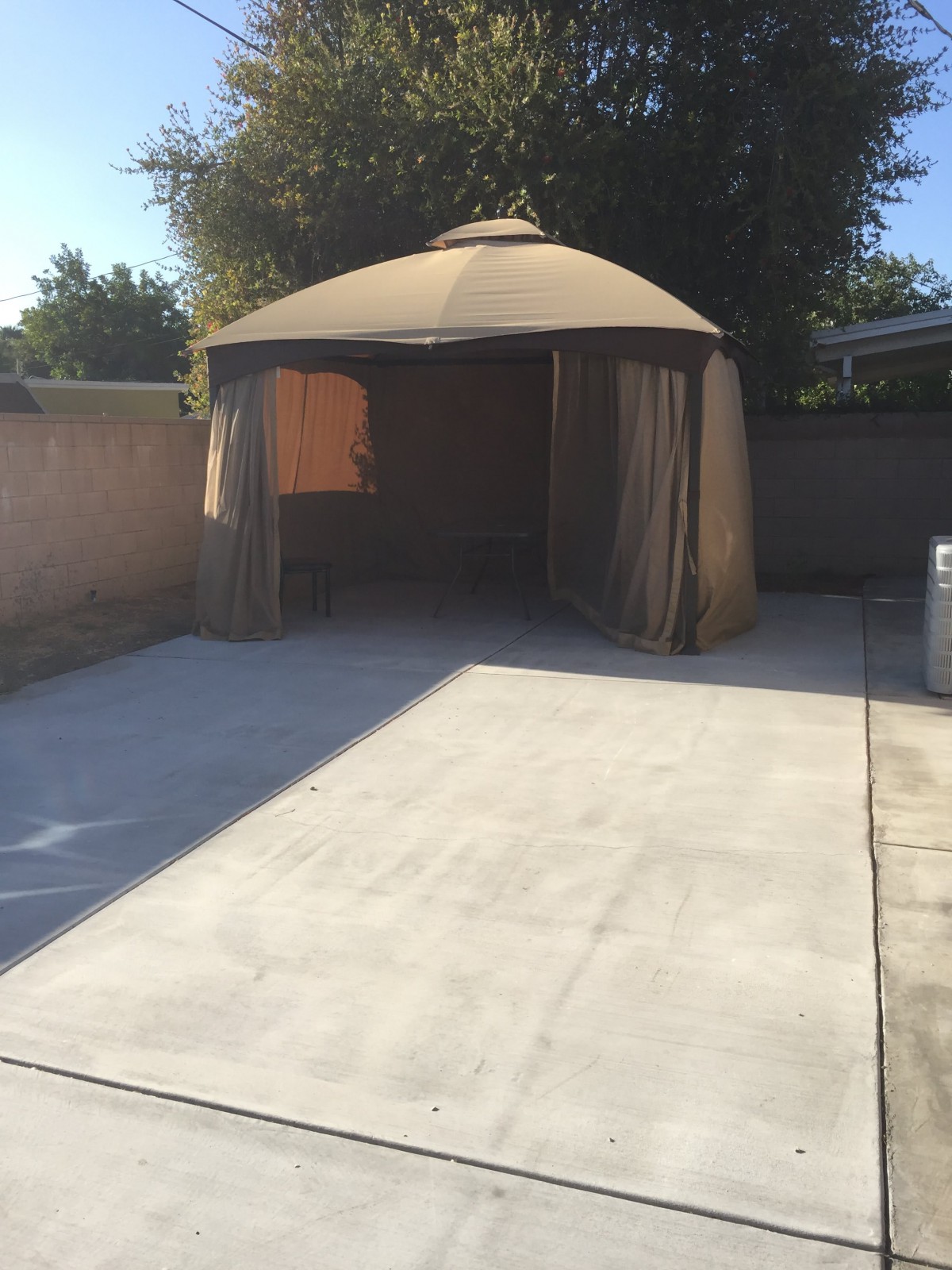 A backyard patio with a gazebo providing shade over a concrete area.