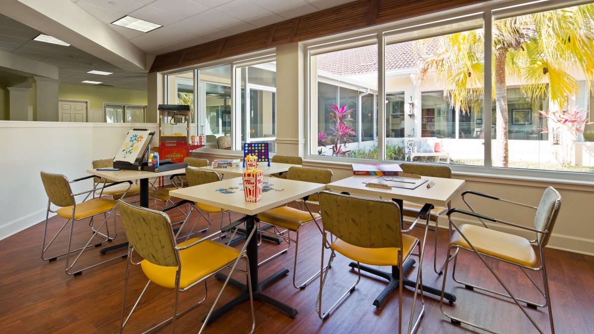 A bright classroom with tables and chairs, featuring large windows letting in natural light.