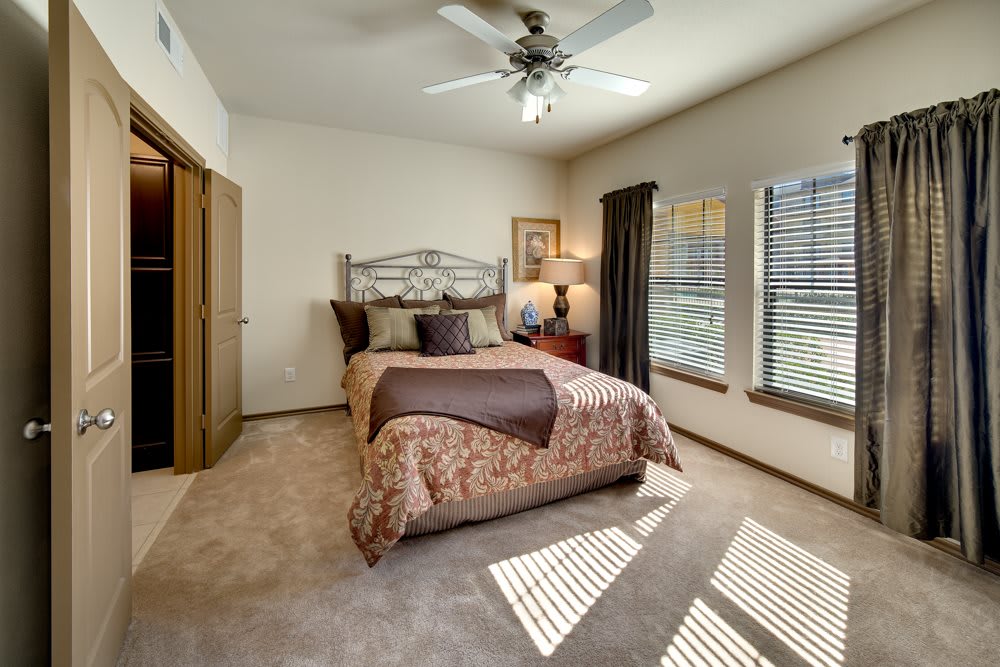 A cozy bedroom with a neatly made bed, ceiling fan, and ample natural light from large windows.