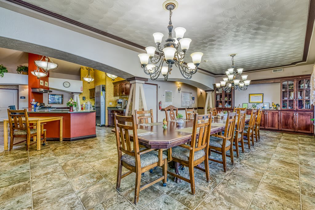 A spacious dining room featuring a long table with wooden chairs and elegant chandeliers.