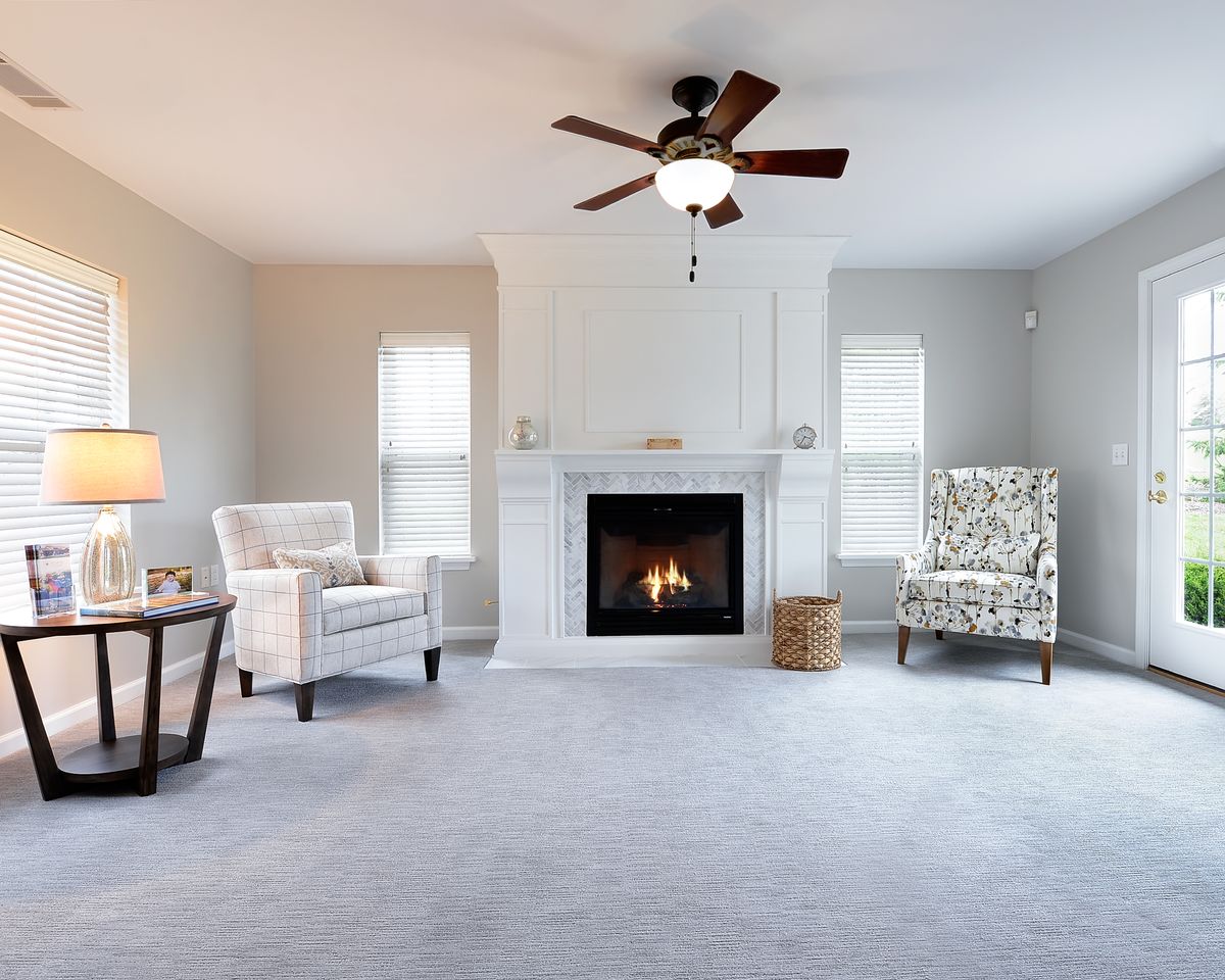 A modern living room with a fireplace, comfortable armchairs, and a ceiling fan.