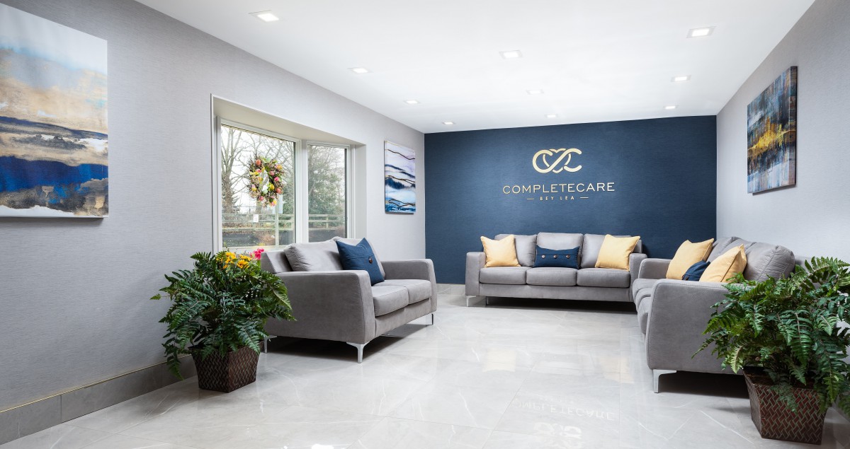 A modern waiting room featuring comfortable sofas, a wall display, and plant decor.