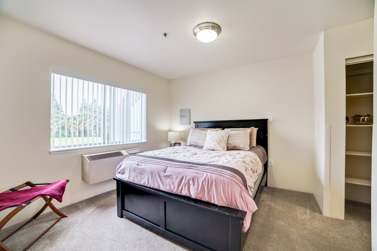 A modern bedroom with a neatly made bed, ample natural light from the window, and simple decor.